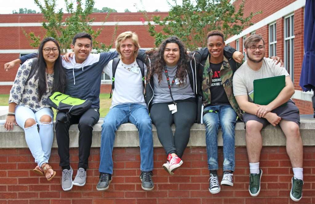Students sitting on a brick wall on campus having fun.
