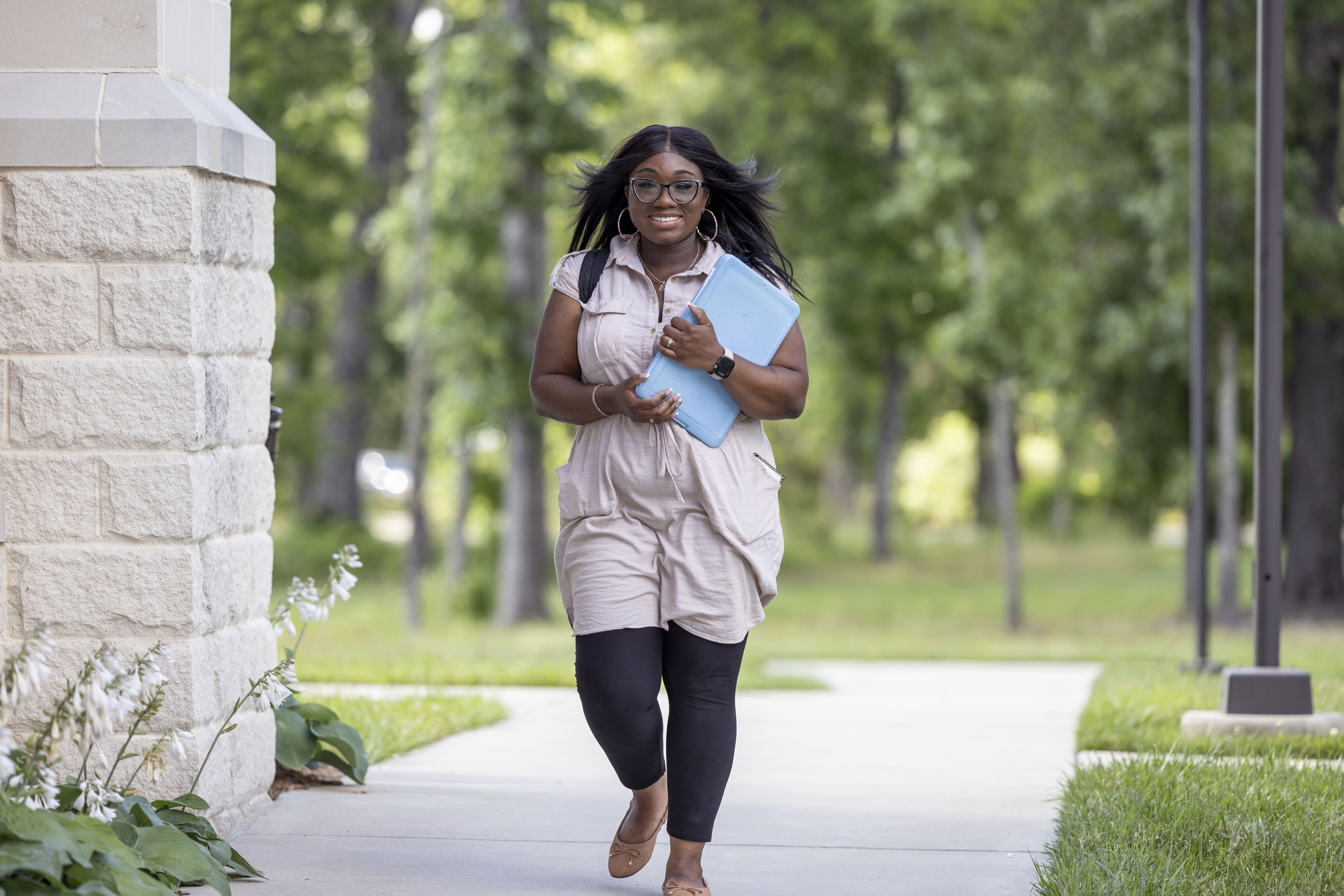 Female student walking outside of campus building, smiling.