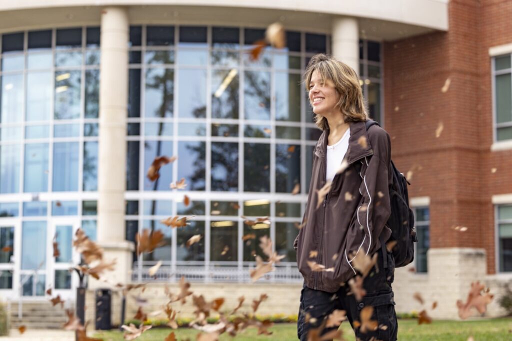 Student walking outdoors by the Main OCH building with the leaves falling in the foreground.