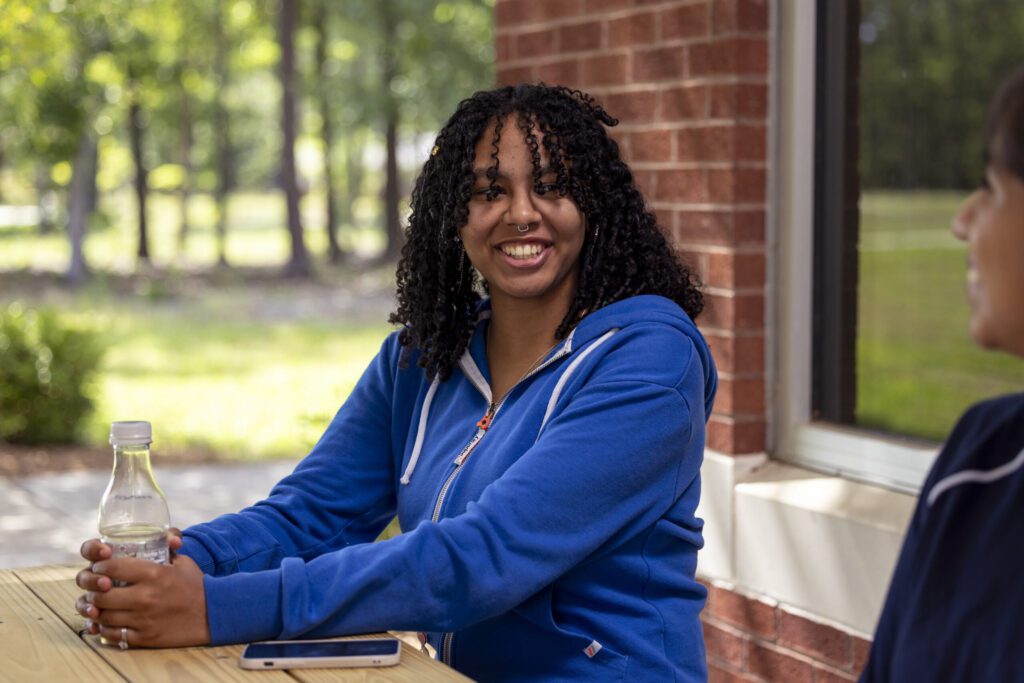 Student sitting outside by a picnic table and smiling.