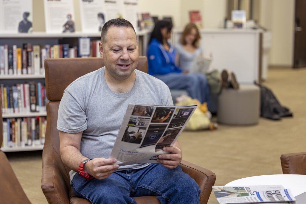 Photo of a male student reading a pamphlet in the South Piedmont library.