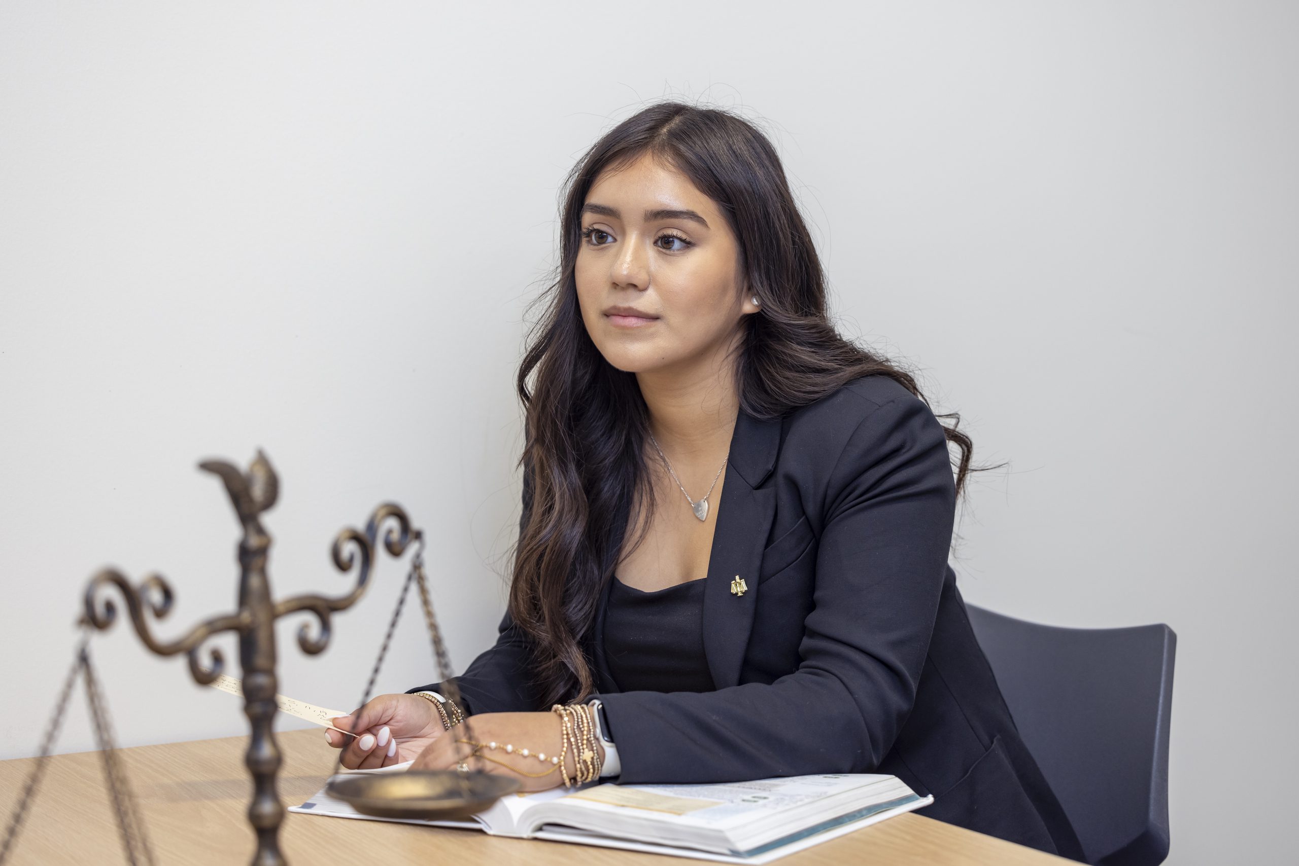 A student dressed in business professional attire seated at a table, with the scale of justice visible nearby.