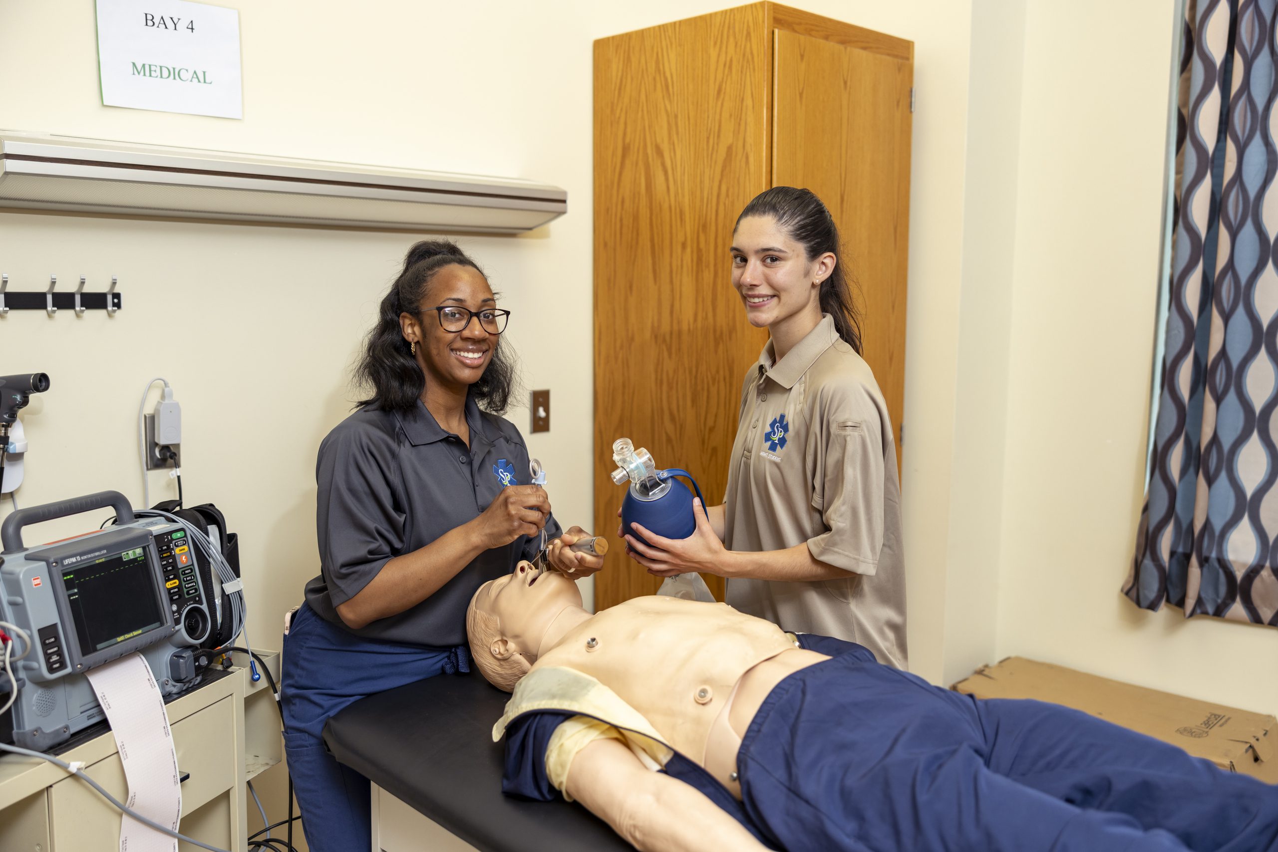 Alt Text: Two female Emergency Medical Science students practicing CPR on manikin.