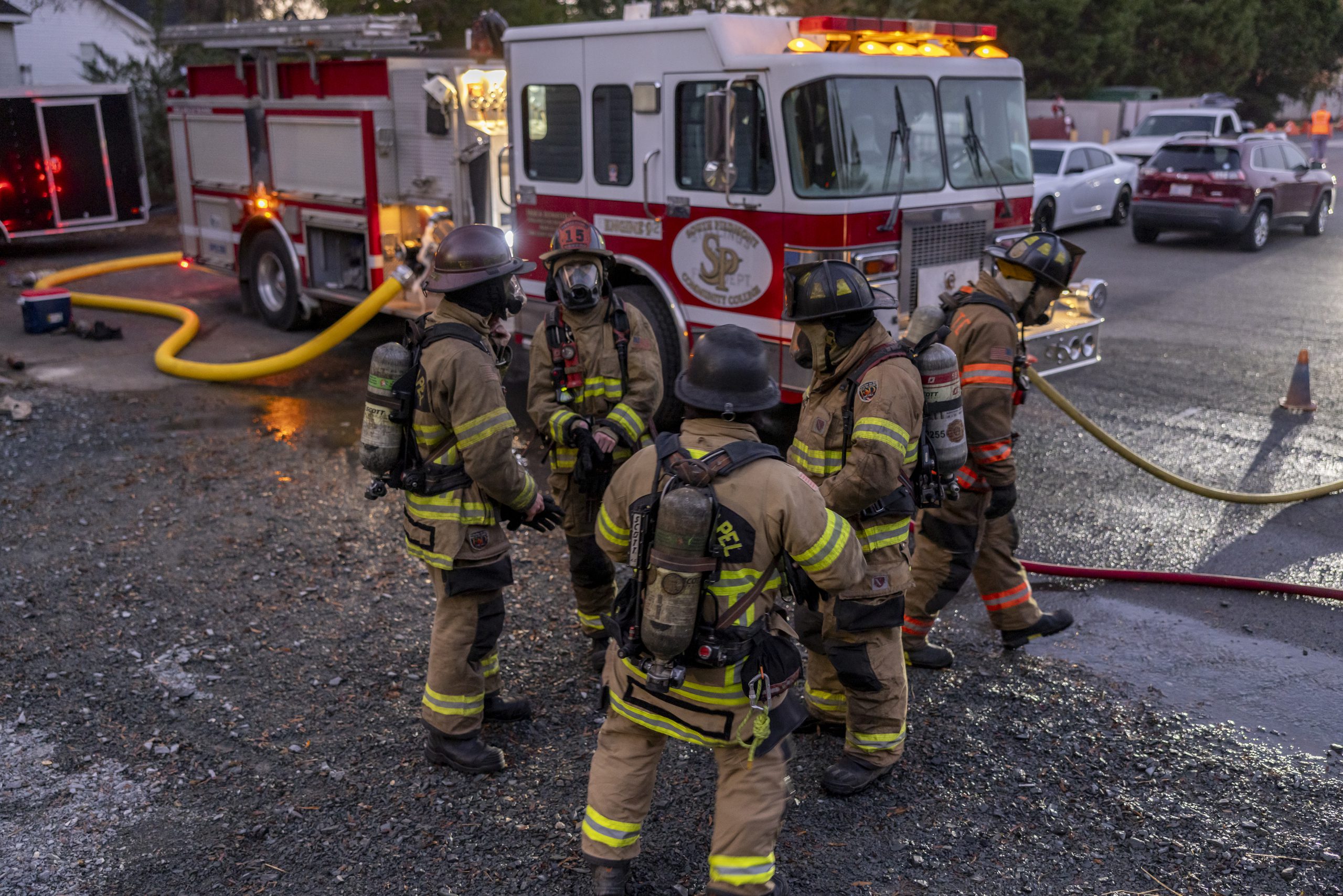 Five firefighters in uniform gathered in a small circle, with a firefighting truck displaying South Piedmont's 'SP' logo visible in the background
