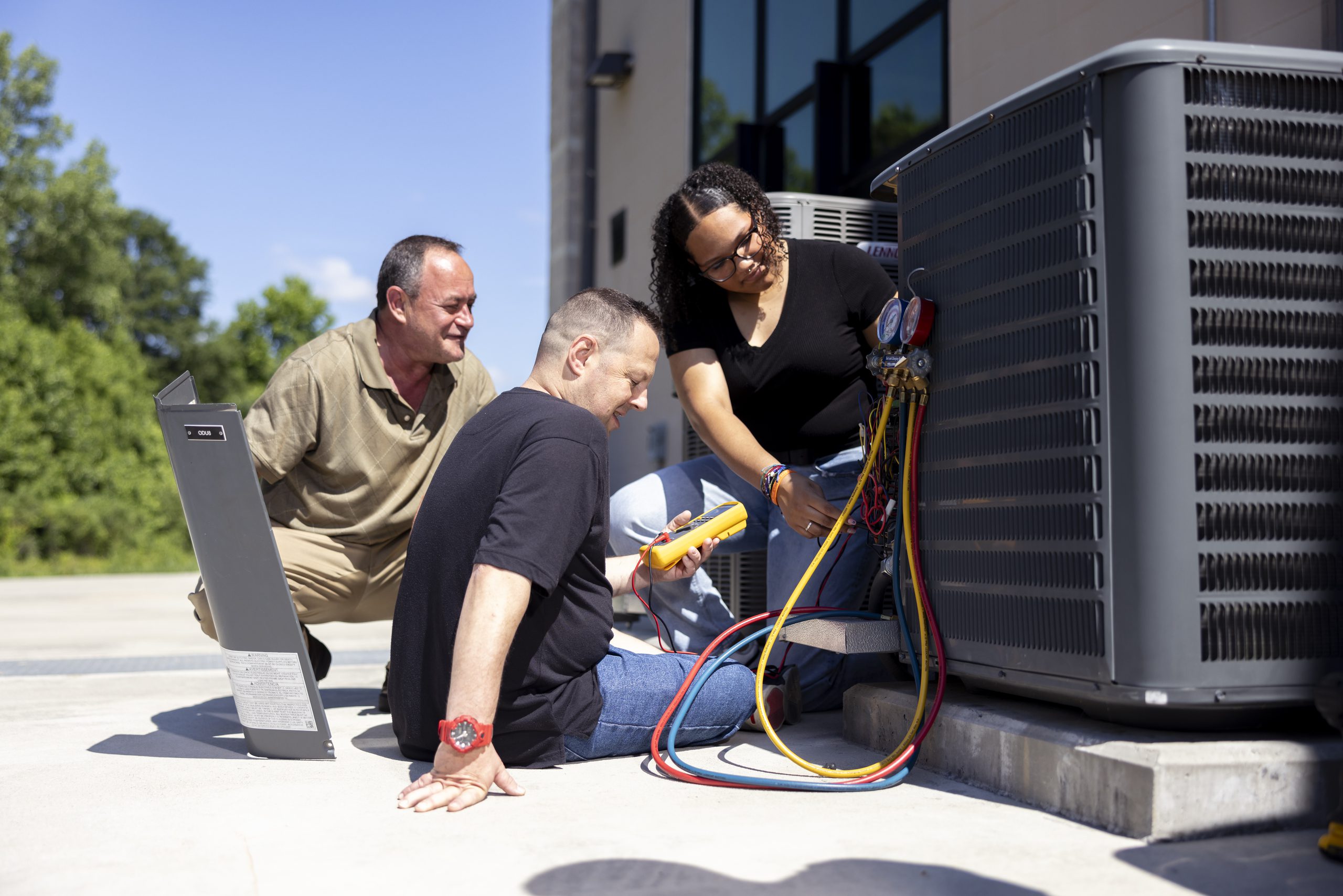 Two students and an instructor inspecting outdoor HVAC equipment, discussing its functionality in an outdoor setting.