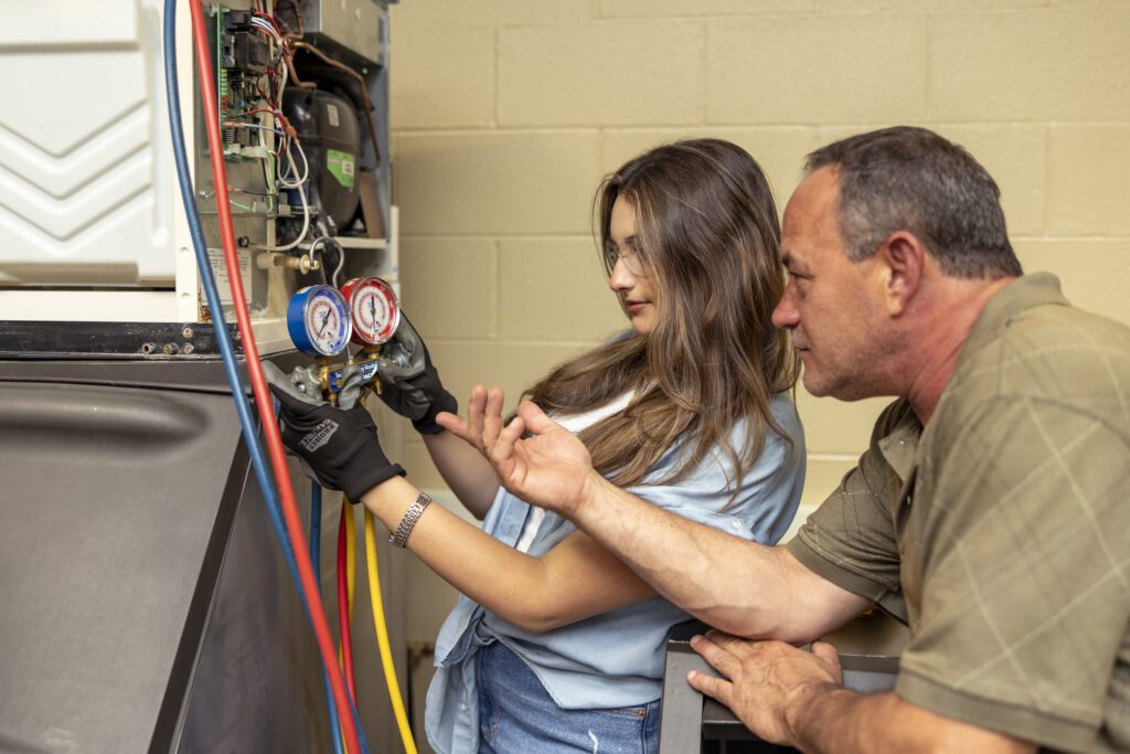A student and an instructor inspecting indoor HVAC equipment, inspecting its components.