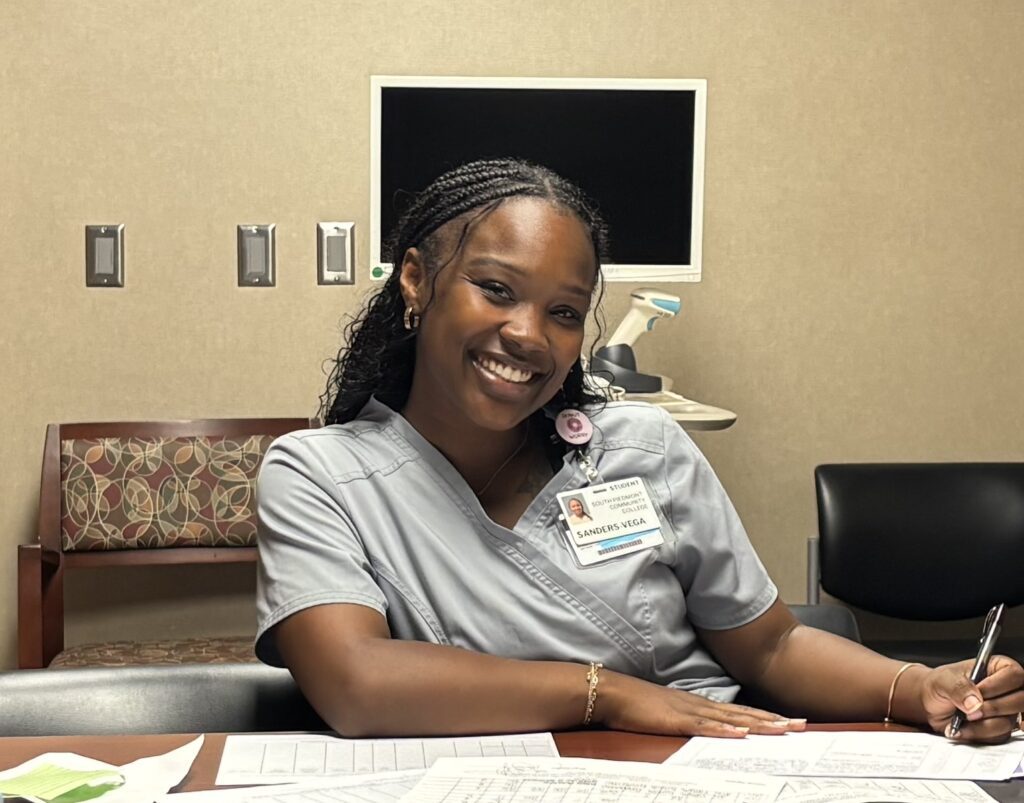 Photo of Jamaria in her gown, smiling at the camera while doing paperwork.