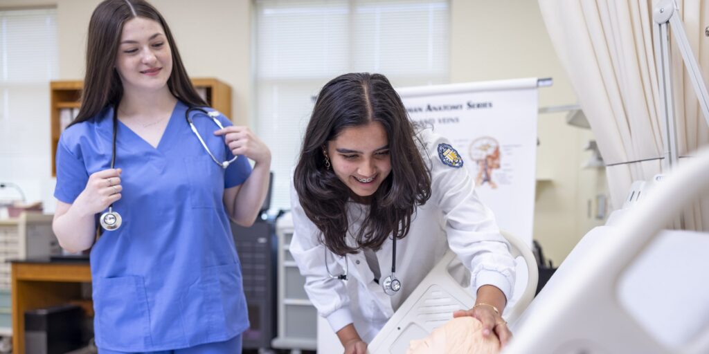 Two female nursing students in scrubs inspecting a medical mannequin.