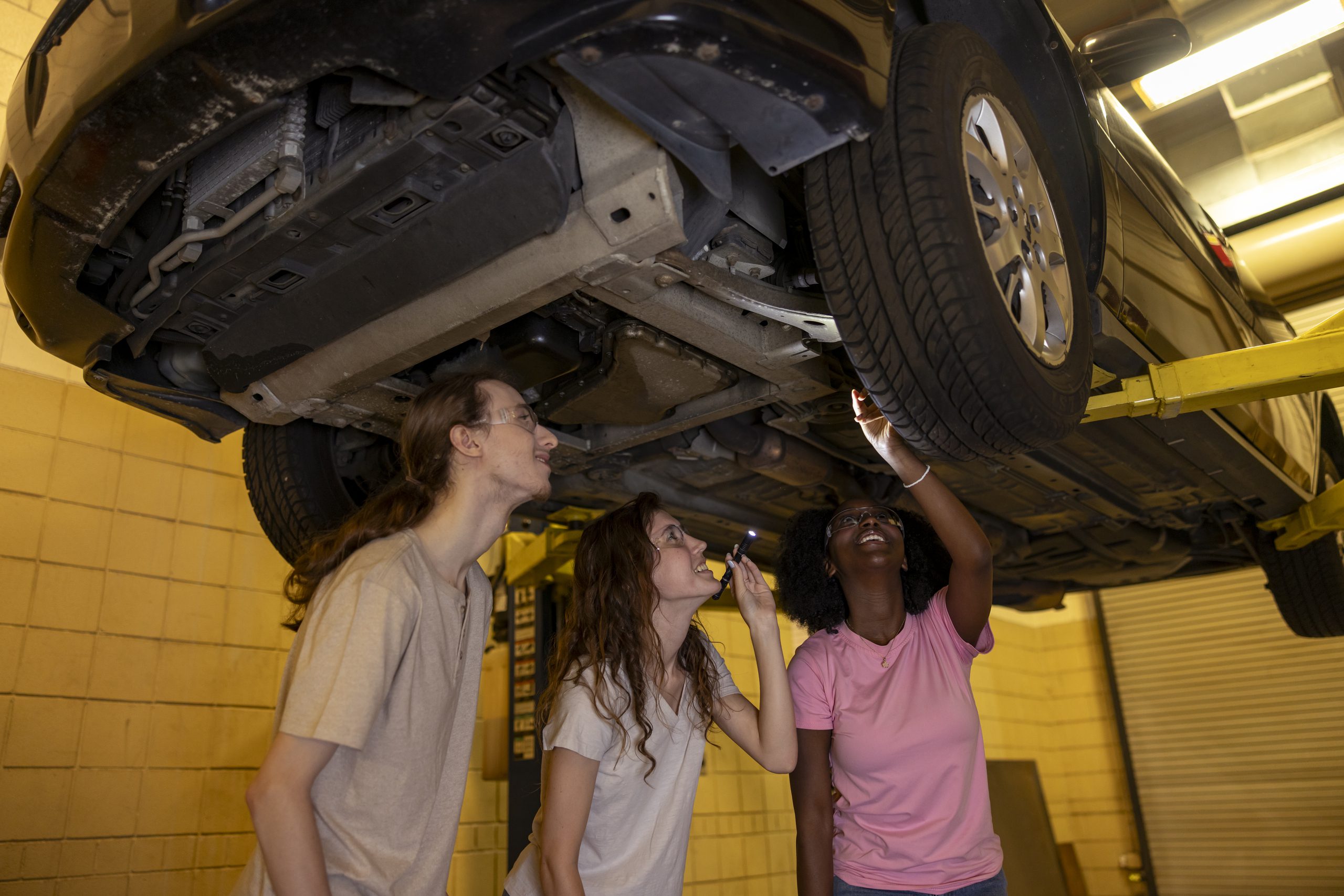Three South Piedmont automotive students inspecting a vehicle's belly pan .