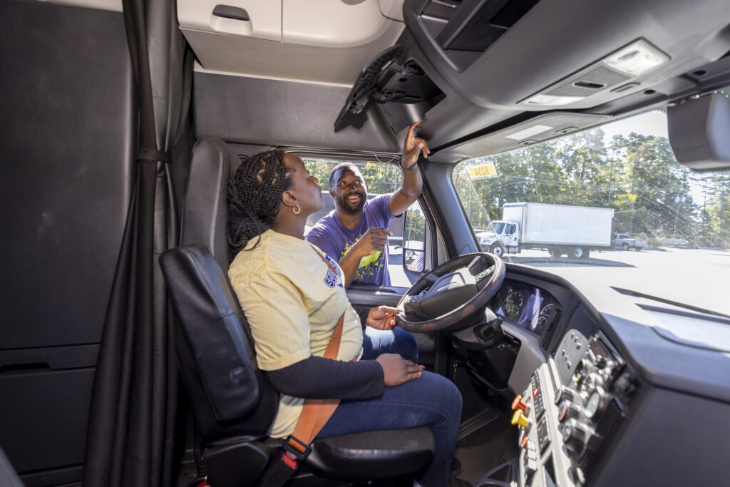 South Piedmont's Truck Driving instructor showing how to operate the truck with a female student sitting on the driver's seat.