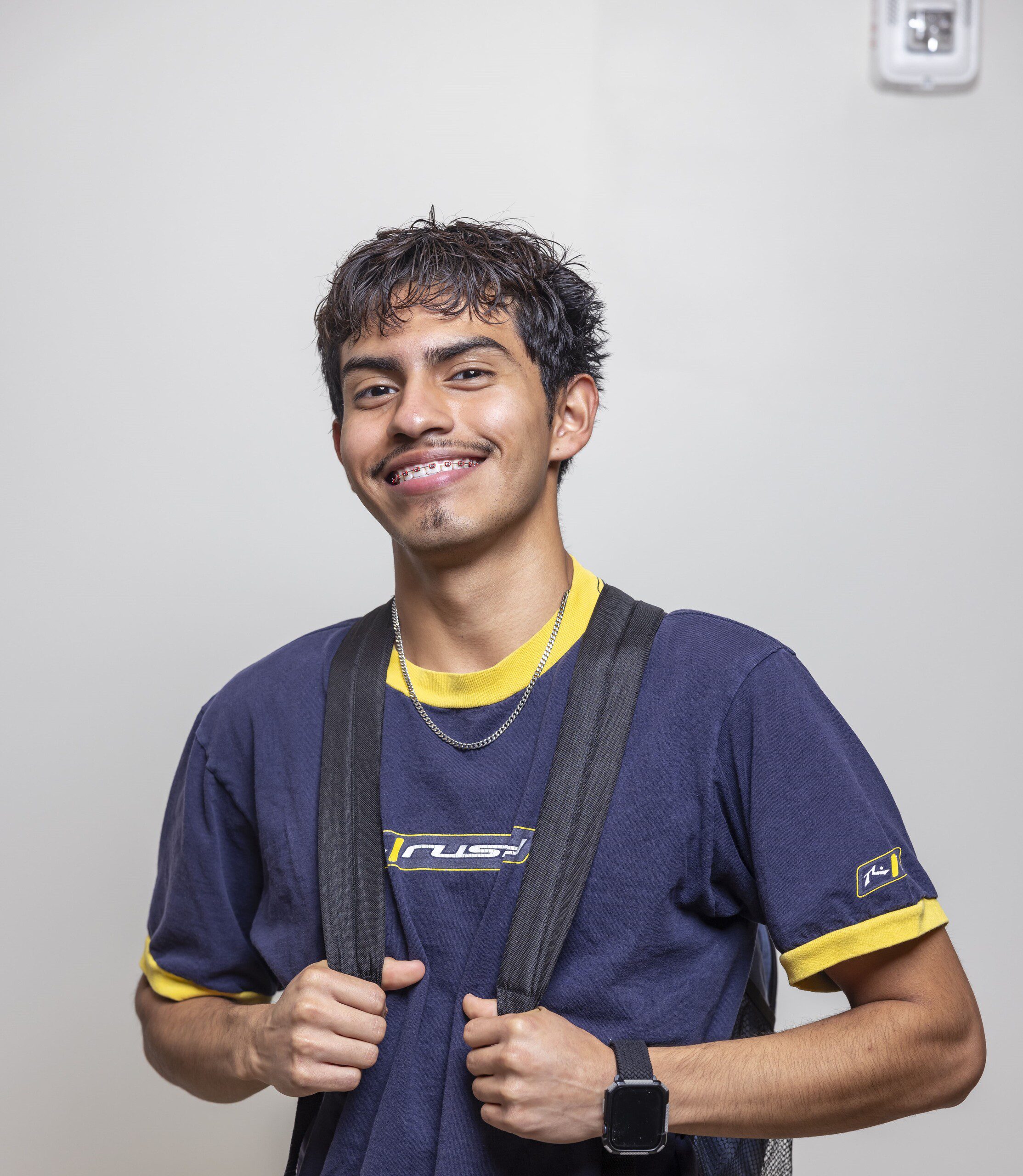 A full shot of a male student standing confidently in a hallway, looking at the camera.