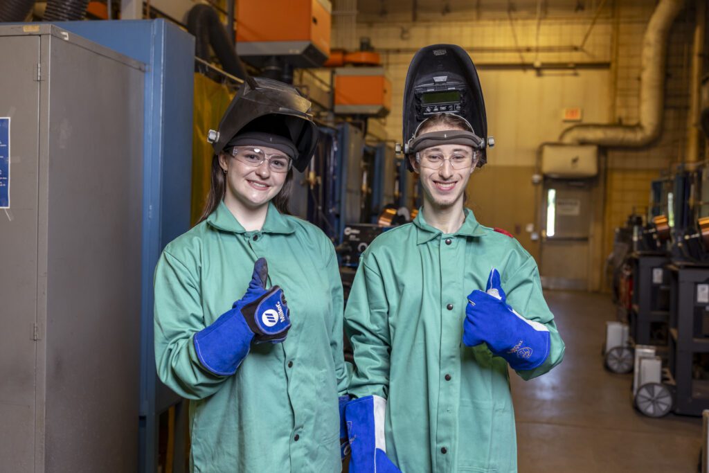 Photo of two South Piedmont students in welding masks and coveralls giving thumbs-up signs.