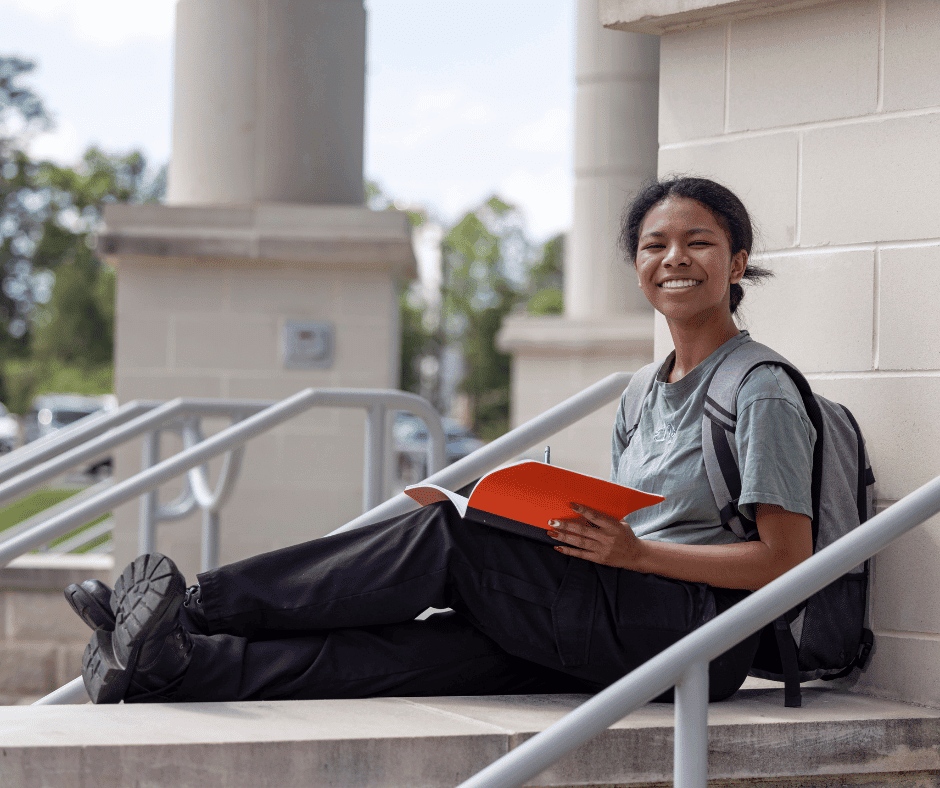 Photo of a female student reading a book outside.