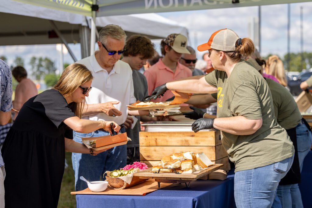 People lined up to make plates of food at an outside event.