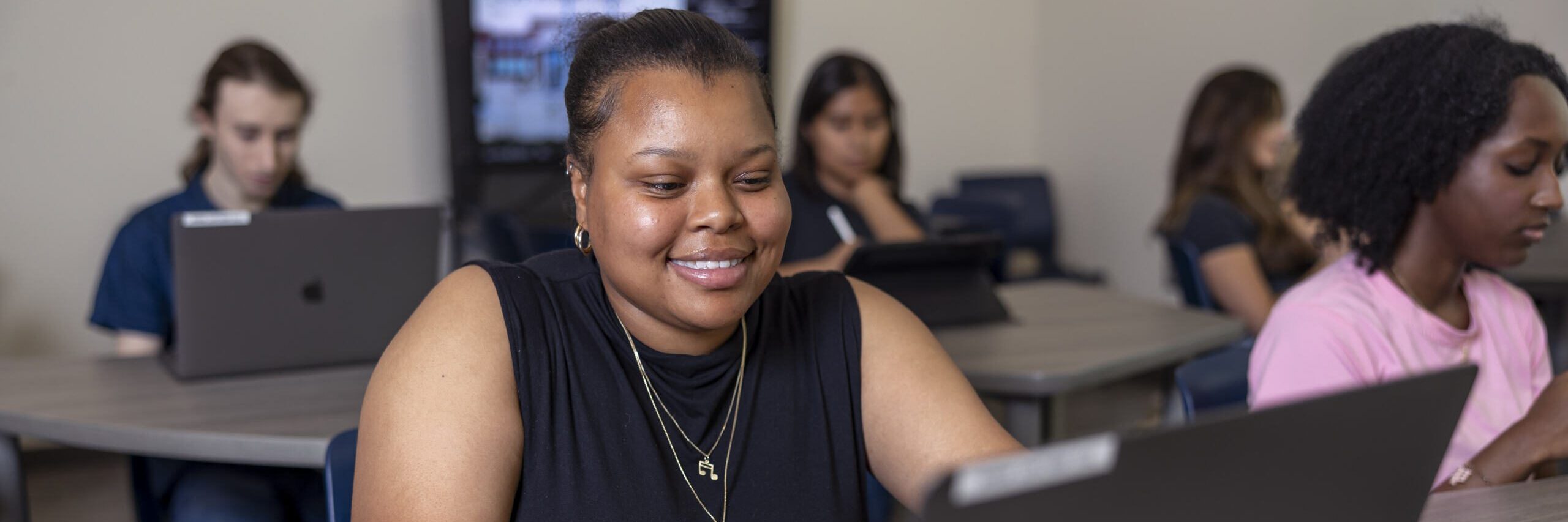 Student smiling in front of a laptop.