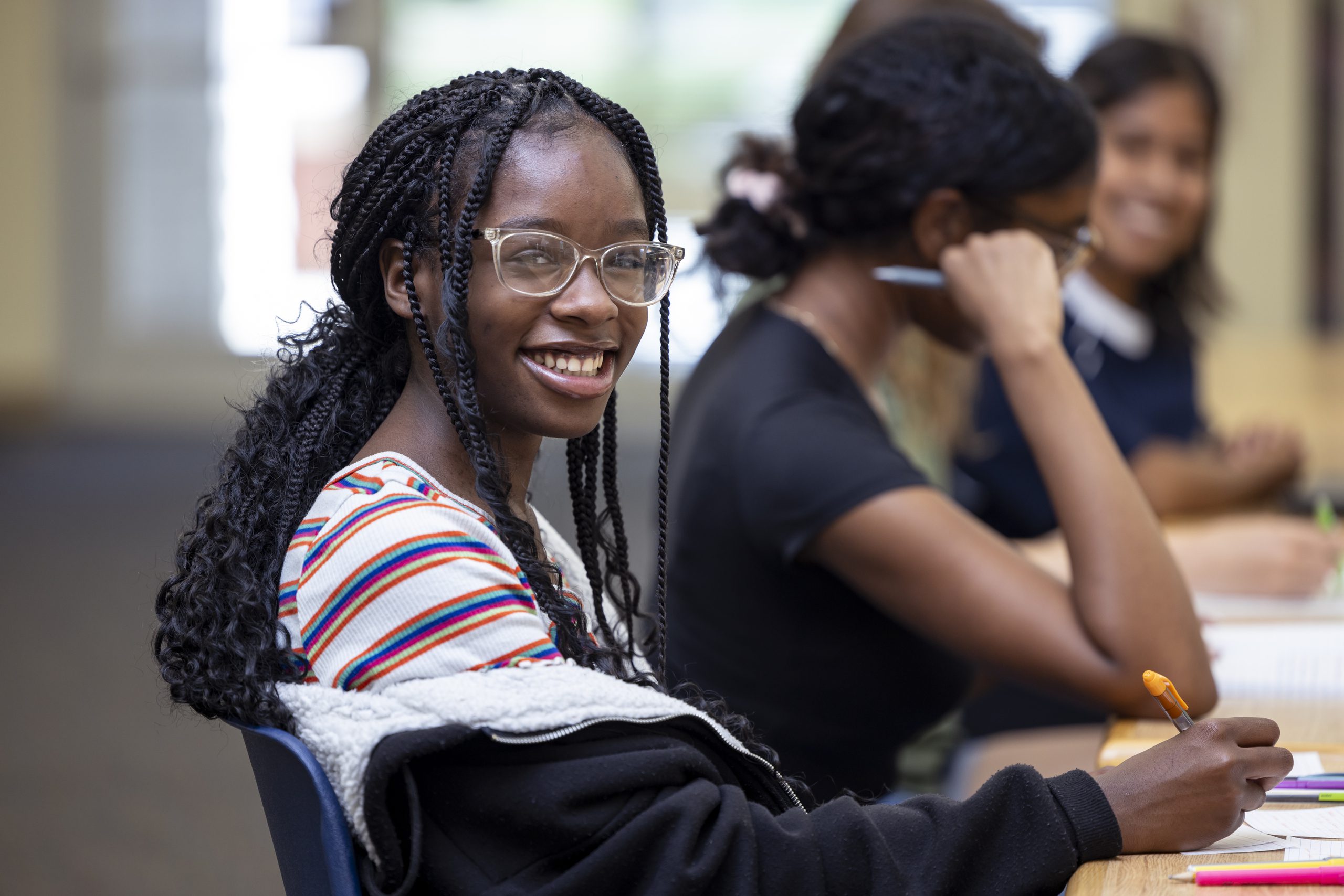 A female student smiling warmly at the camera, momentarily looking away from her group study session.