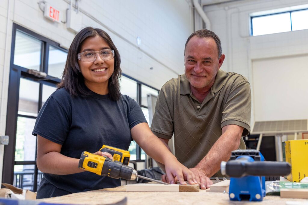 Female student with a drill and her male professor.