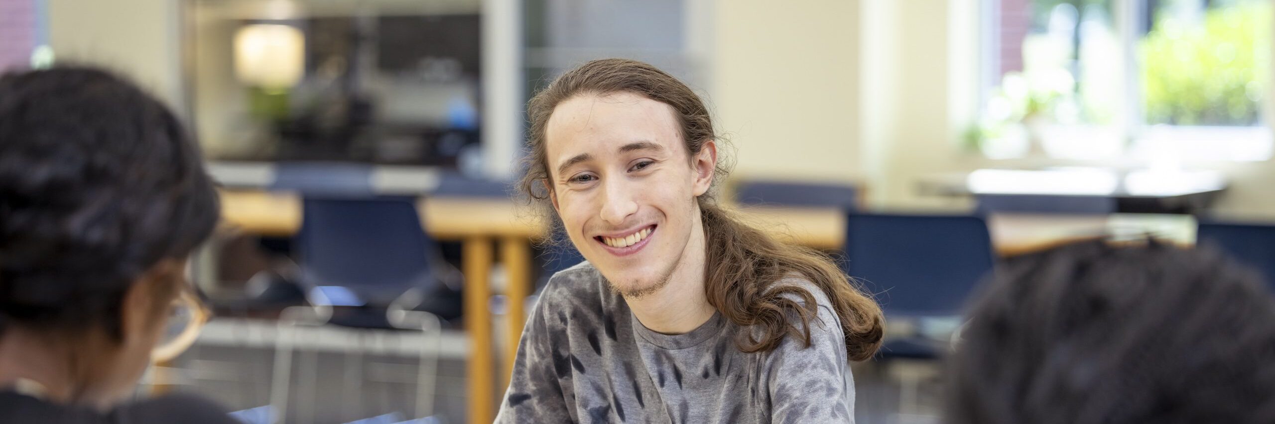 A male student with a ponytail smiling at the camera.