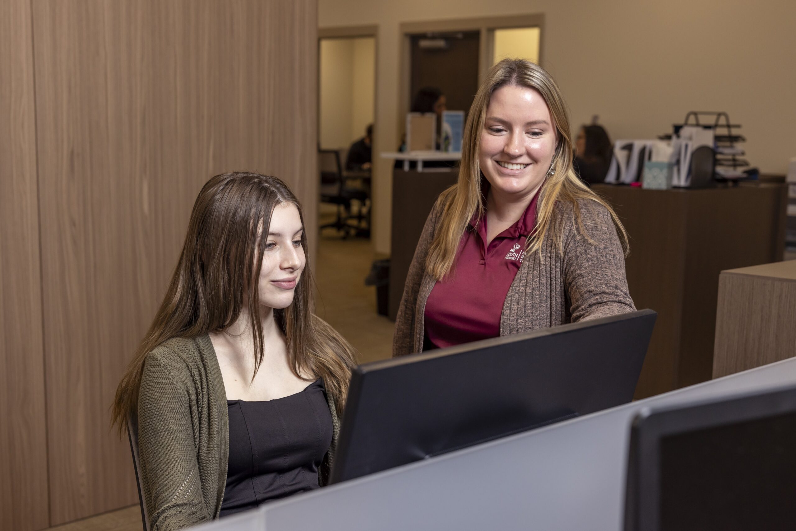 A female employee helping a female student at a computer.