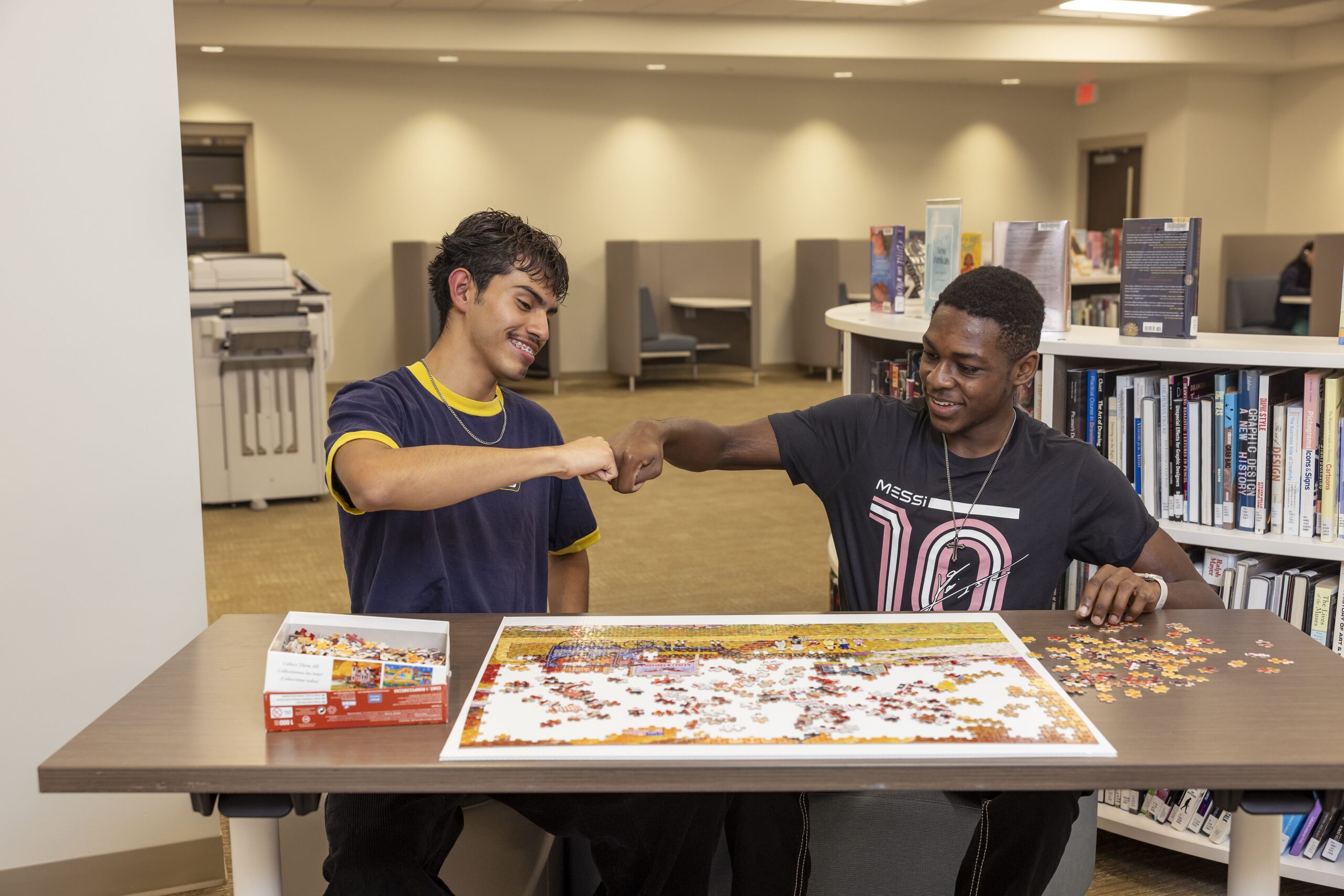 Two male students fist-bumping each other while putting together a puzzle.