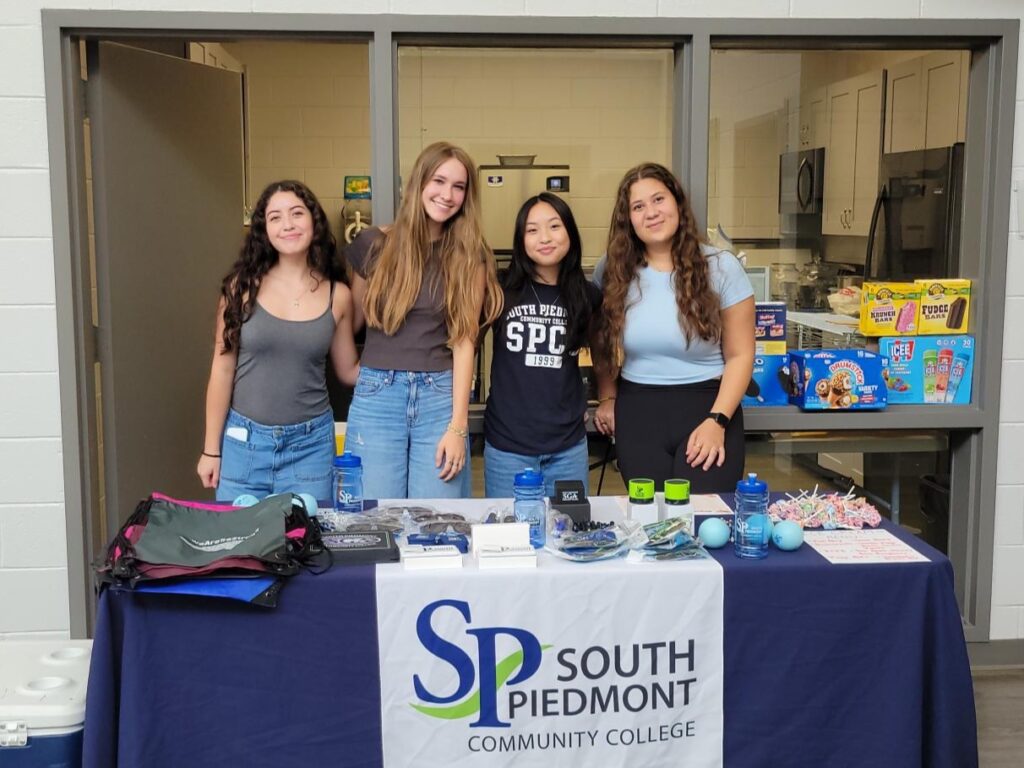 A group of students standing around a table themed with South Piedmont signs and brochures.