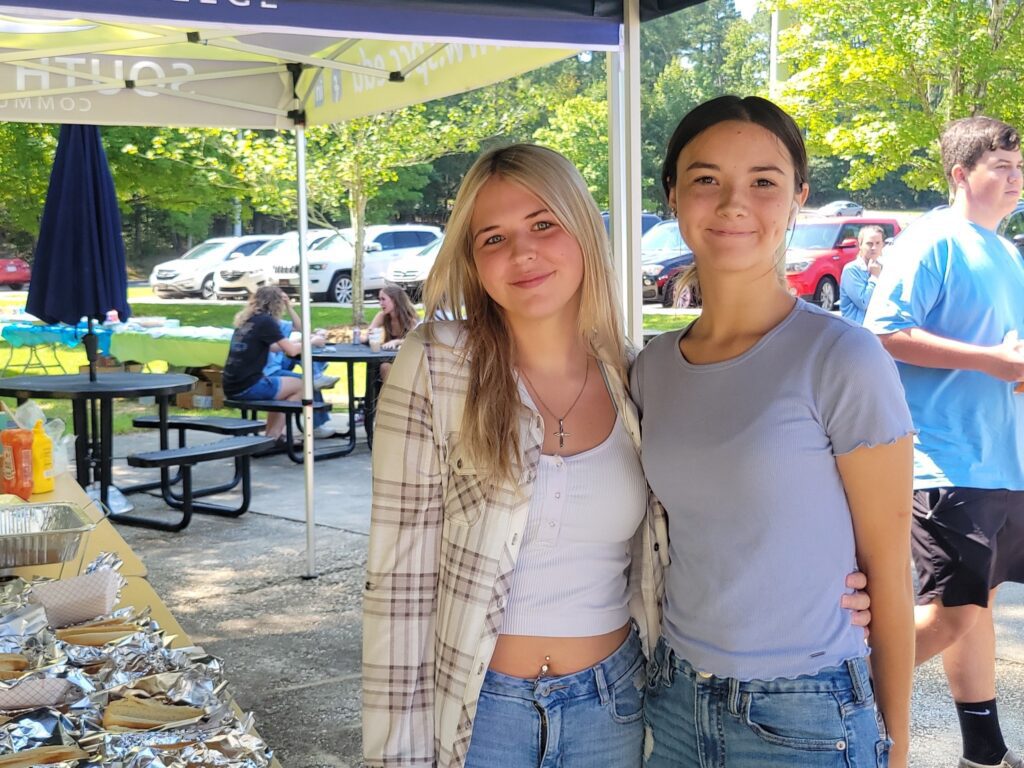 Photo of two girls standing next to a stack of hot dogs.