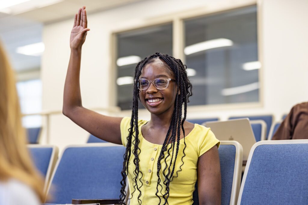 A female student in a yellow shirt raising her hand.