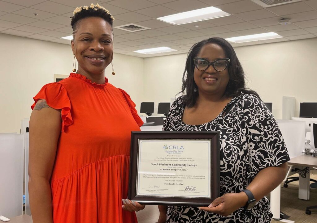 Two women holding a certificate inside a computer lab.
