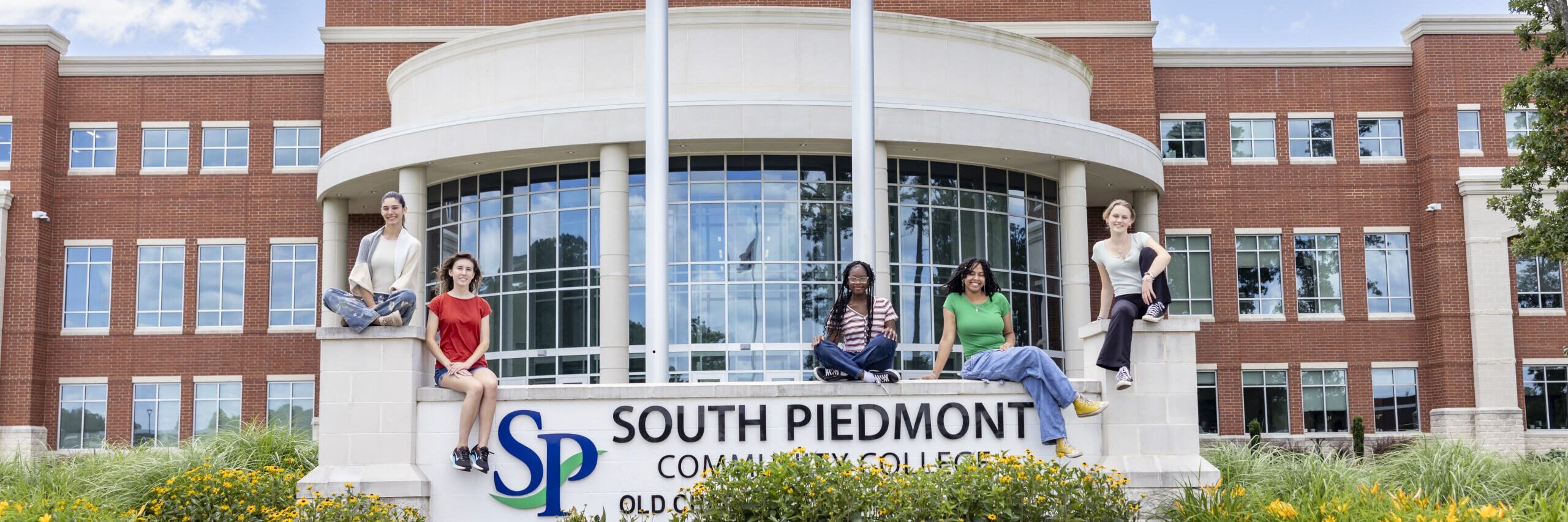 Photo of several students sitting on the sign outside the South Piedmont Old Charlotte HIghway campus.
