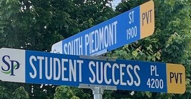 Two street signs, one that reads South Piedmont Street, another that reads Student Success Place.