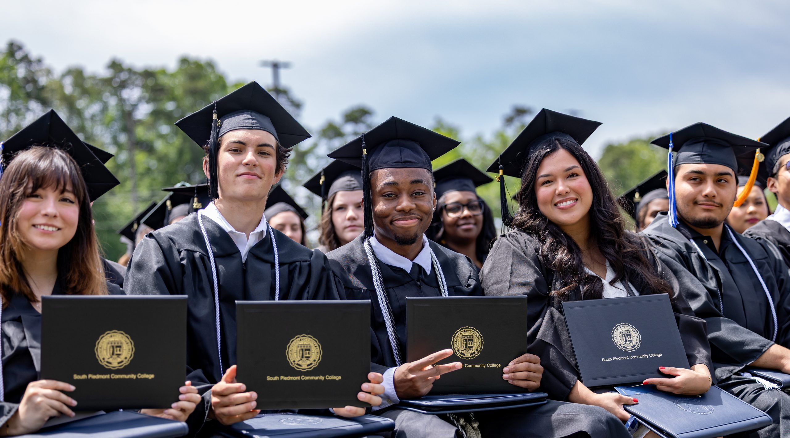 Group of recent graduates sitting and holding up their diploma.