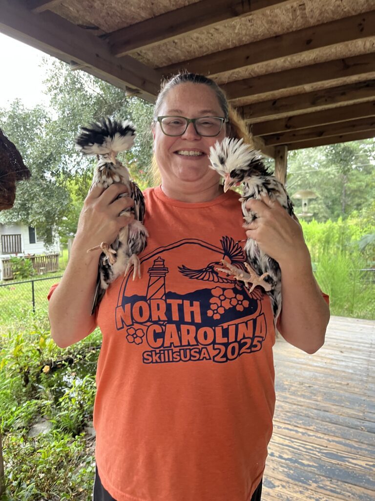 A woman in an orange shirt holding two chickens. 