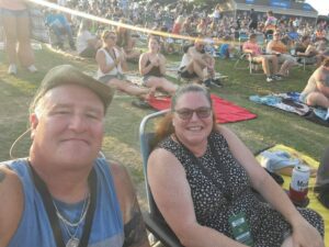 Two people in lawn chairs at an outdoor concert. 
