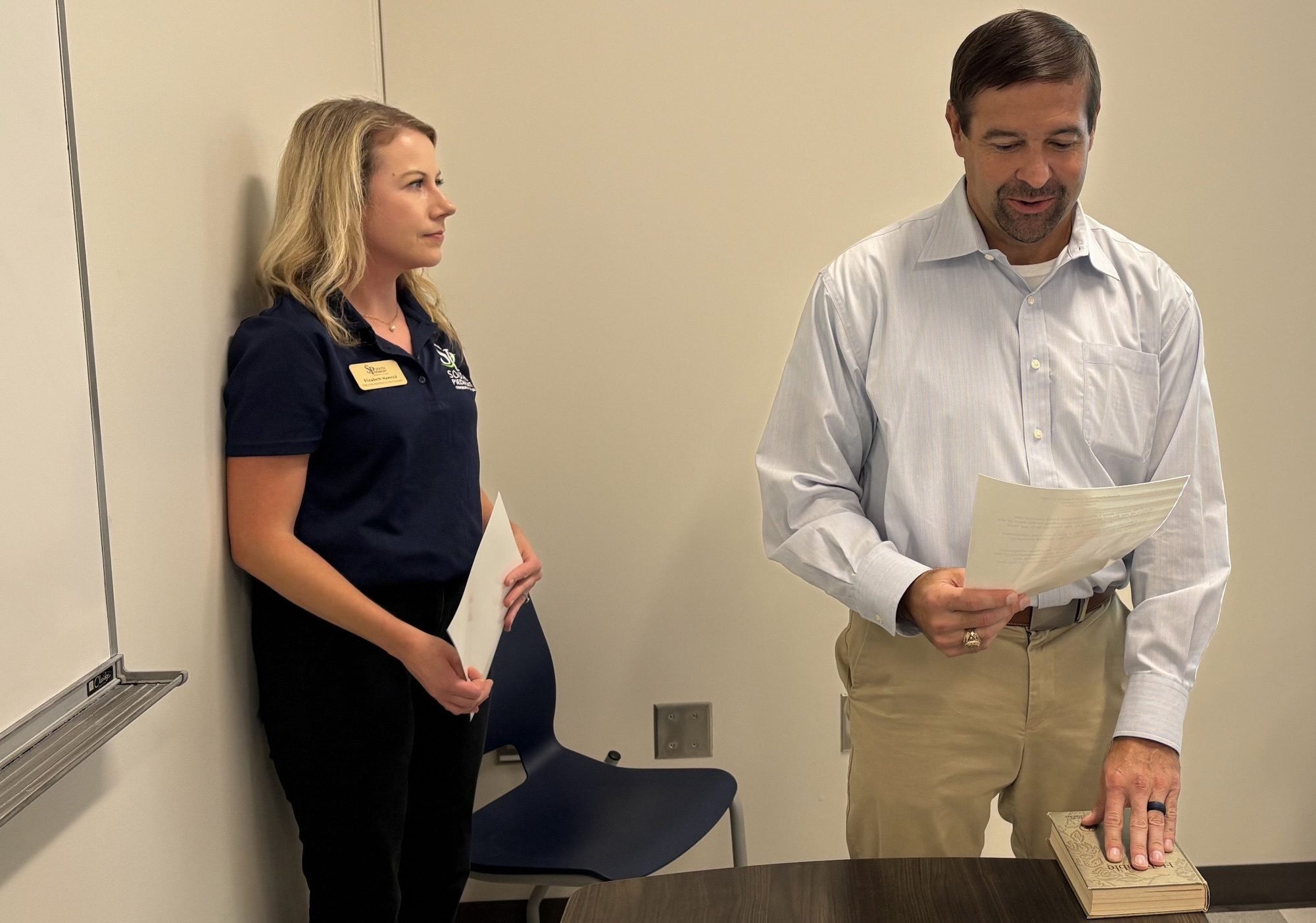 A woman giving the oath of office to a new Board of Trustees member.