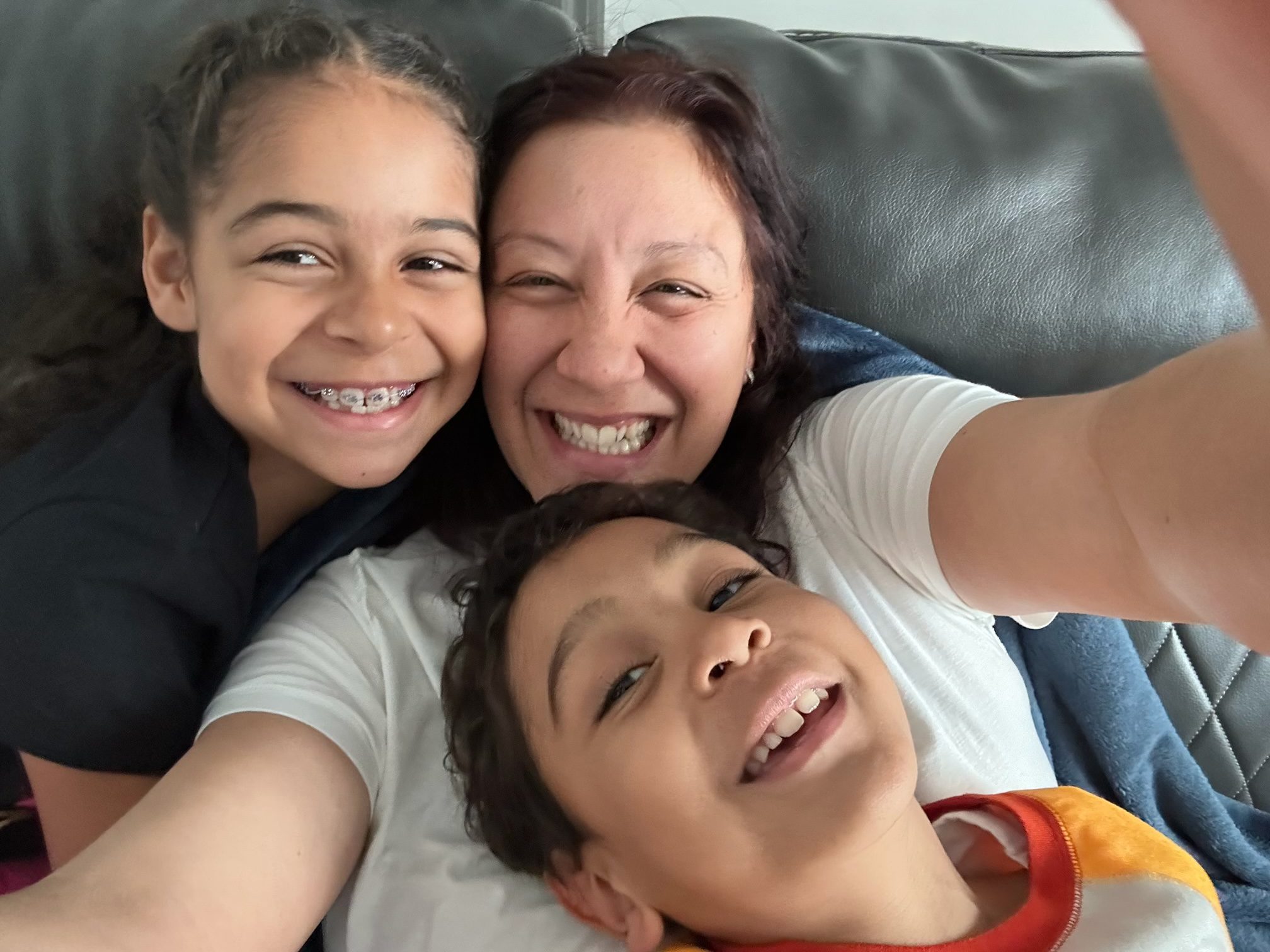 A woman with her two young children, posing for a photo on their couch.