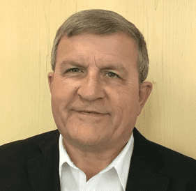 Older gentleman wearing a white button up and black suit jacket.