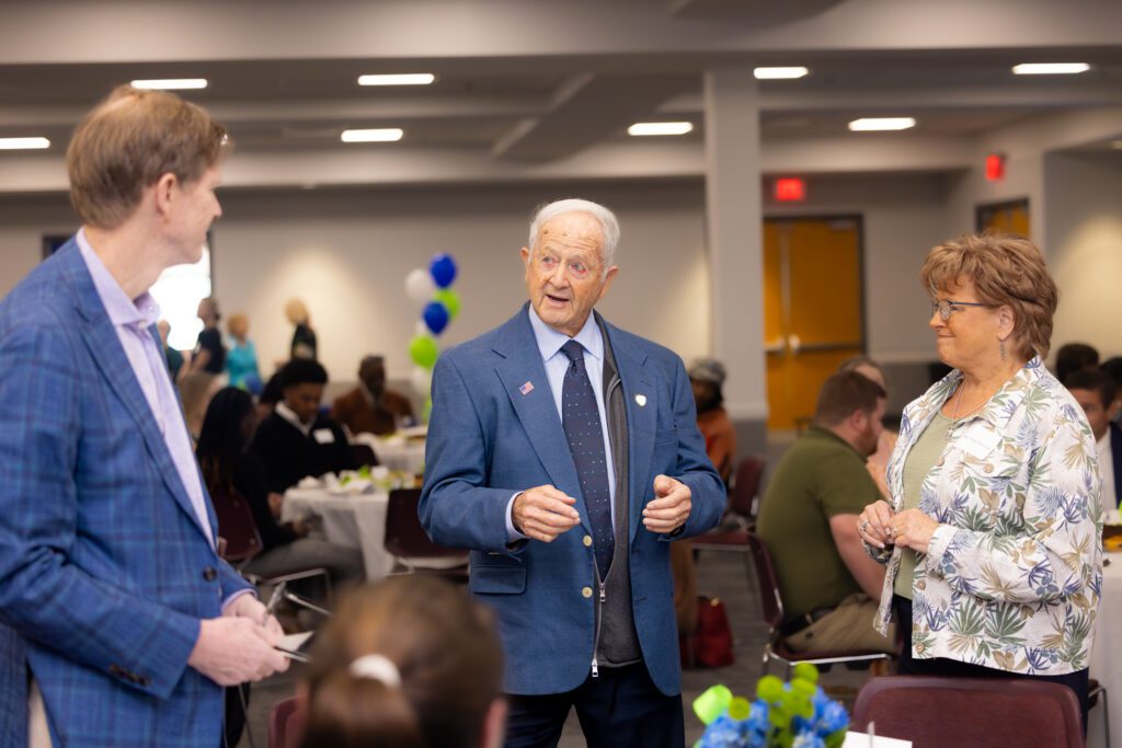 Three people, dressed in business formal, enjoy a conversation during the Scholarship Luncheon event at South Piedmont Community College.