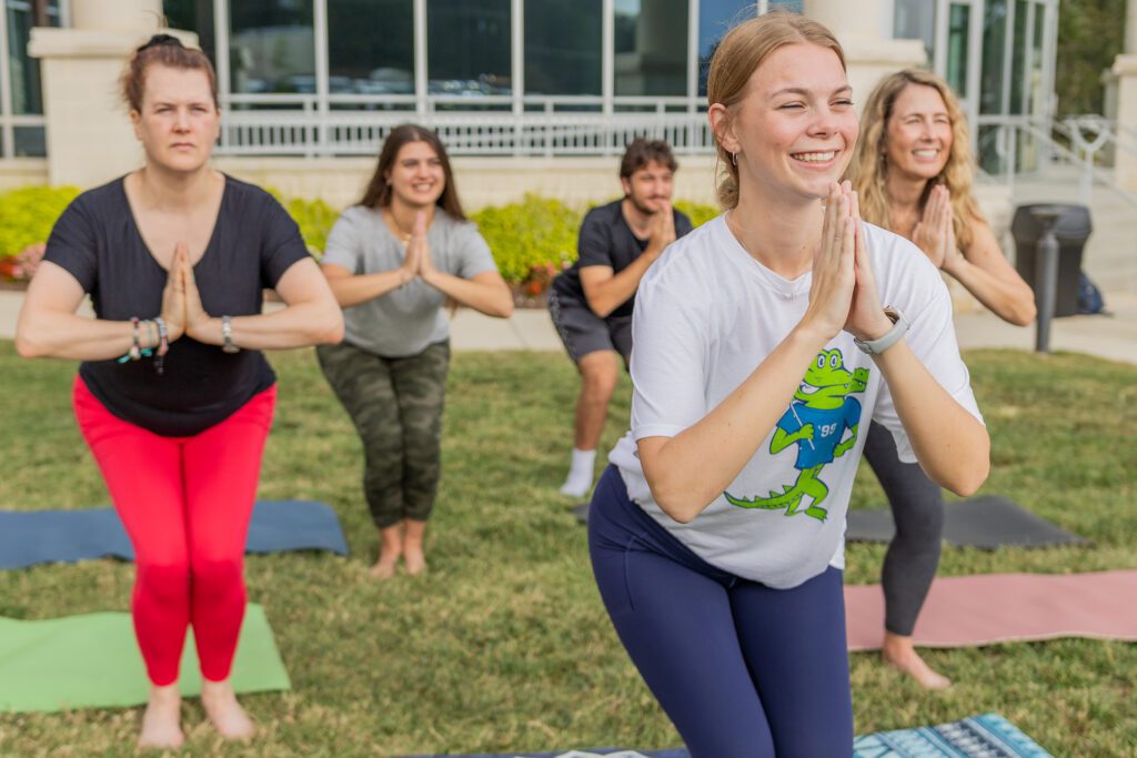 Groups of people practice yoga outside of South Piedmont's OCH Main building.