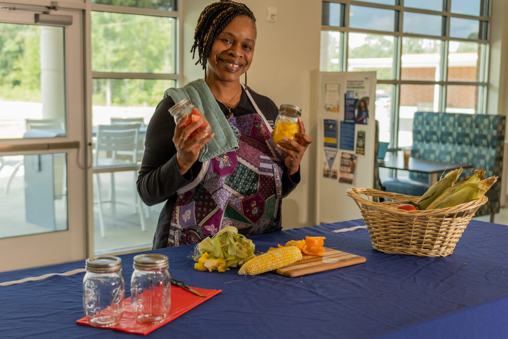 Woman holds up jars of fruits with vegetables laid out in front of her.