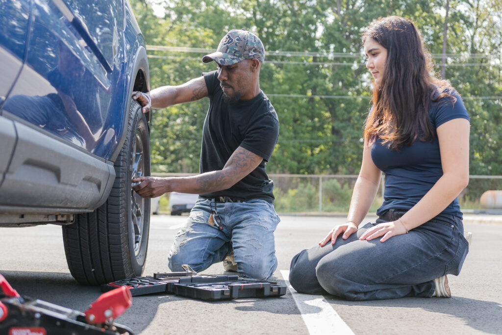 Two people go practice their automotive maintenance skills on a blue vehicle.