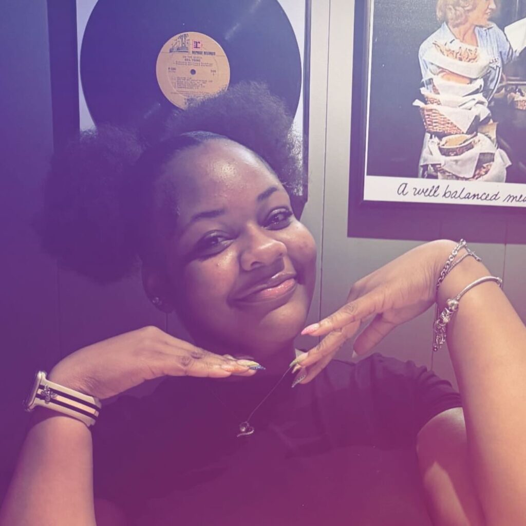 Photo of Zialyn Clark indoors, smiling at the camera with her hands up.