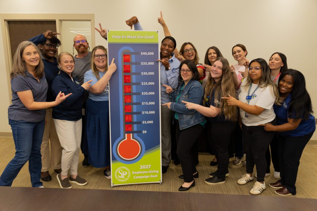 Group of people surrounding the Employee Giving Campaign Goal banner.
