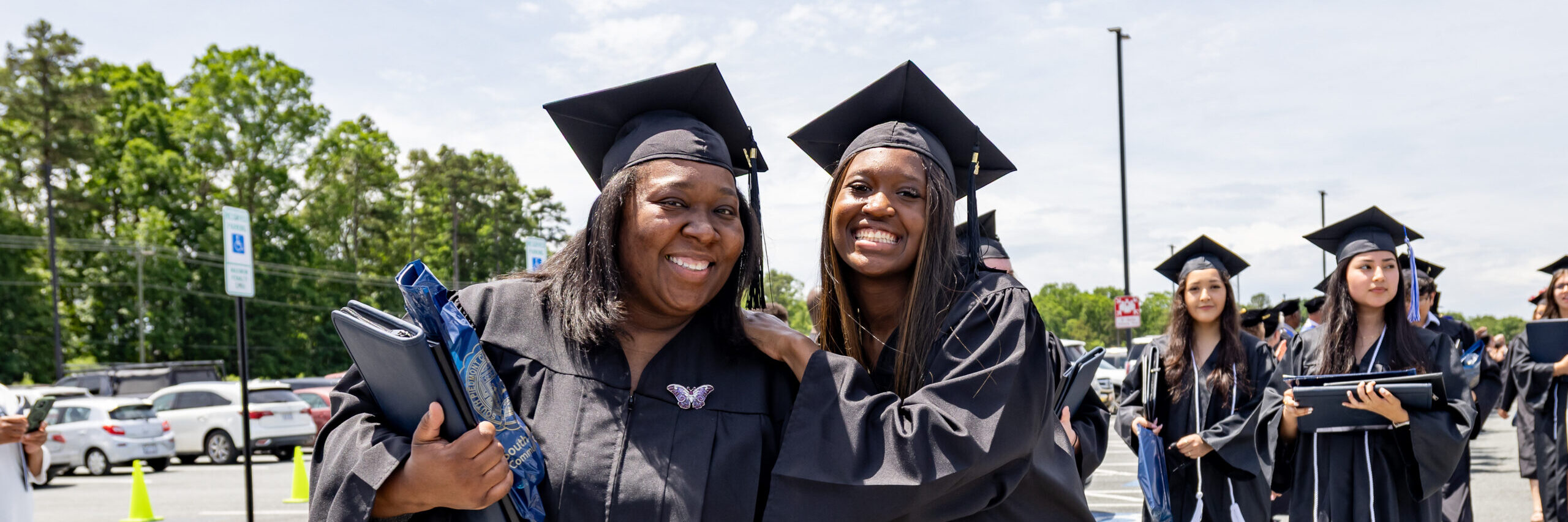 Two South Piedmont graduates dressed in graduation gowns smile at the camera on graduation day.